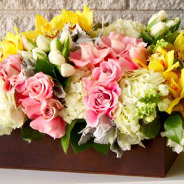 Pink roses and yellow orchids arranged in a rectangular box with white blooms