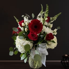 Red roses and white flowers in a glass vase with a sheer ribbon