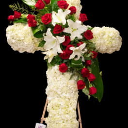 Cross-shaped floral tribute with red roses, white lilies, and white hydrangeas