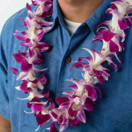 Purple and white orchid lei worn around a person's neck over a blue shirt