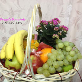 Fruit basket with bananas, grapes, oranges, apples, and a potted pink flowering plant