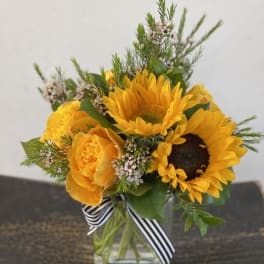 Yellow sunflower and rose bouquet in a glass vase with a striped ribbon
