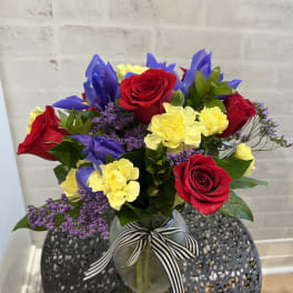 Bouquet of red roses, yellow carnations, and purple flowers in a glass vase