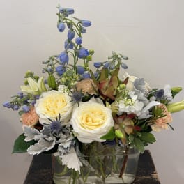Mixed bouquet in a clear glass vase with cream roses and blue flowers