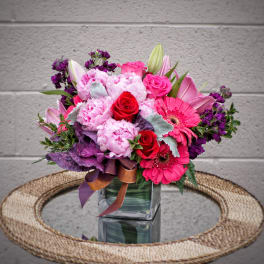 Pink and purple bouquet in a square glass vase with ribbon