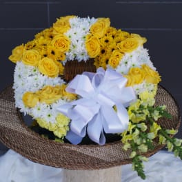 Yellow roses and white daisies arranged in a woven basket with a white ribbon bow.