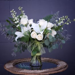 White lilies and roses arranged in a glass vase with greenery