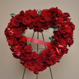 Heart-shaped red rose wreath on a stand with a ribbon
