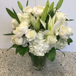 White floral bouquet in a clear glass vase with lilies, roses, and hydrangeas