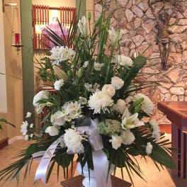 Tall white floral arrangement in a white vase with a ribbon bow