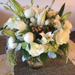 White floral arrangement in a glass vase with roses and lilies