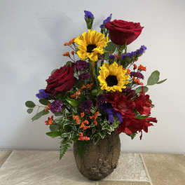 Mixed bouquet with red roses, sunflowers, and red alstroemeria in a rustic vase