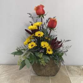Arrangement of red roses and yellow daisies in a round wooden container