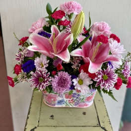 Pink lilies and mixed flowers in a floral tin container