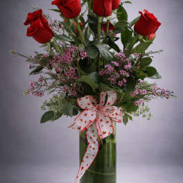 Red roses in a glass vase with a heart-patterned ribbon