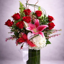 Red roses and a pink lily in a tall glass vase with ribbon