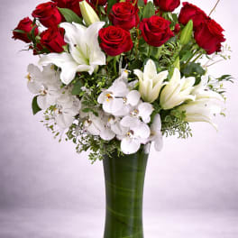 Red roses and white lilies with orchids in a tall green vase