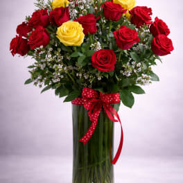 Bouquet of red and yellow roses in a clear glass vase with a red ribbon