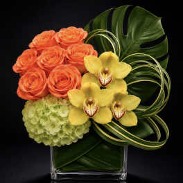 Orange roses, yellow orchids, and green hydrangea in a clear square vase