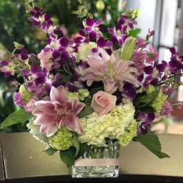 Pink lilies, roses, hydrangeas, and purple orchids in a clear glass vase