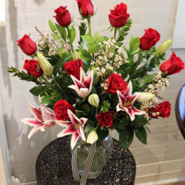 Red roses and pink lilies arranged in a glass vase with a striped ribbon.
