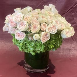 Blush pink roses arranged in a clear glass vase with green hydrangea