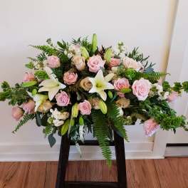 Pink roses and white lilies arranged in a low, wide display on a stand