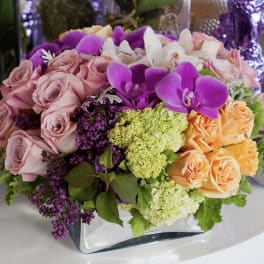 Mixed bouquet of pink roses, purple orchids, and white flowers in a glass vase