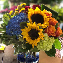 Bouquet with sunflowers, blue hydrangea, and orange roses in a glass vase