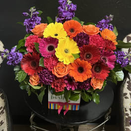Bright mixed bouquet with gerbera daisies, roses, and purple blooms in a gift box