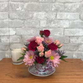Pink and red rose bouquet in a floral teacup with a saucer