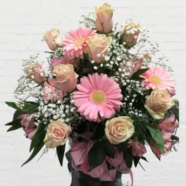 Pink gerbera daisies and pale roses in a vase with baby's breath