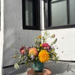 Mixed bouquet of bright orange, pink, and purple flowers in a teal vase