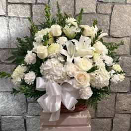 White floral arrangement with roses, lilies, and chrysanthemums in a basket with a ribbon