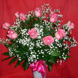 Pink roses and baby's breath in a white vase with a pink ribbon