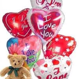 Heart-shaped balloons with love messages and a teddy bear