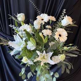 White floral arrangement in a clear glass vase with lilies and daisies
