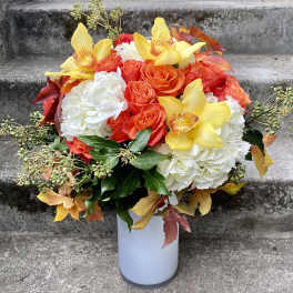 Bouquet of orange roses, white hydrangeas, and yellow orchids in a white vase