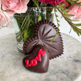 Pink flowers in a glass vase with two heart-shaped chocolates in front