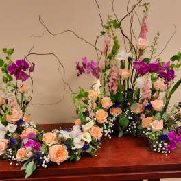 Floral arrangement with peach roses, white lilies, and purple orchids