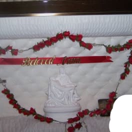 Red rose garland framing a white quilted casket interior with a crucifix