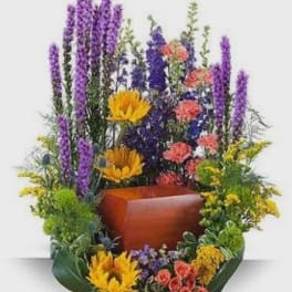 Tall mixed floral arrangement with purple spikes, yellow blooms, and coral flowers in a wooden container