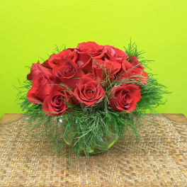 Red roses arranged in a low glass vase with airy greenery