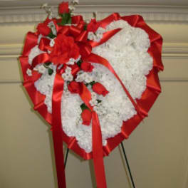 Heart-shaped white floral wreath with red roses and ribbon on an easel