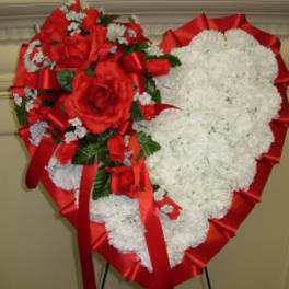 Heart-shaped floral tribute with red roses and white flowers on a stand