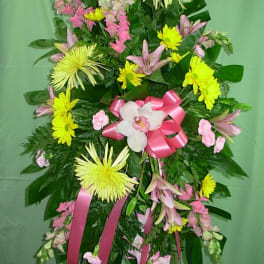 Standing floral spray with pink and yellow flowers and a pink ribbon bow