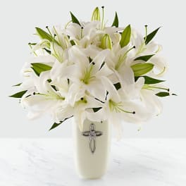White lily bouquet in a cream vase with a silver cross