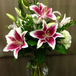 Pink stargazer lilies and white flowers in a glass vase
