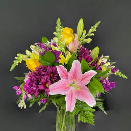Pink lily and mixed purple-yellow flowers in a clear glass vase