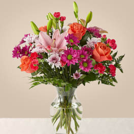 Mixed bouquet of pink lilies, roses, and daisies in a clear glass vase